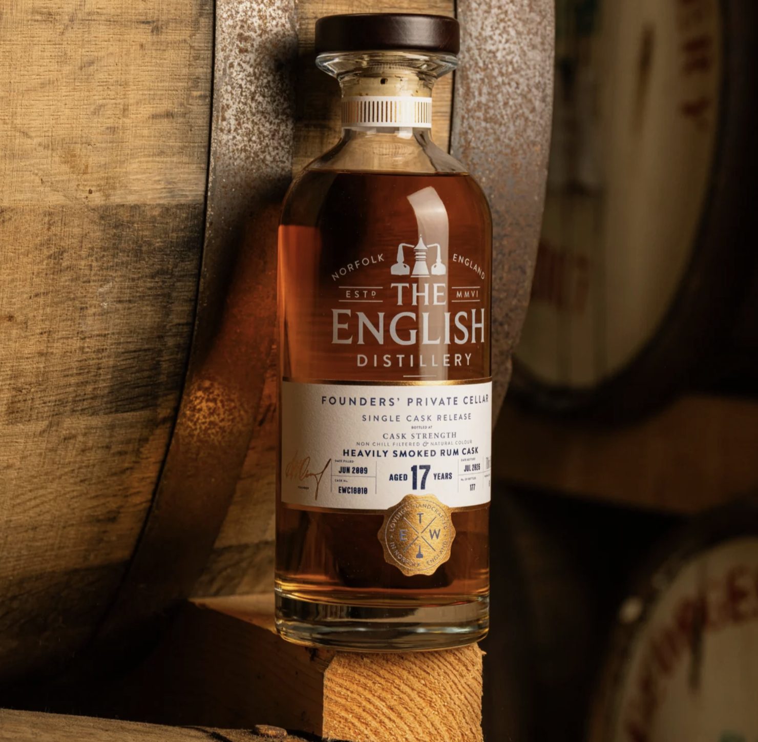 The English 17 Year Old Heavily Smoked Rum Cask bottle resting against casks in the distillery warehouse in Norfolk
