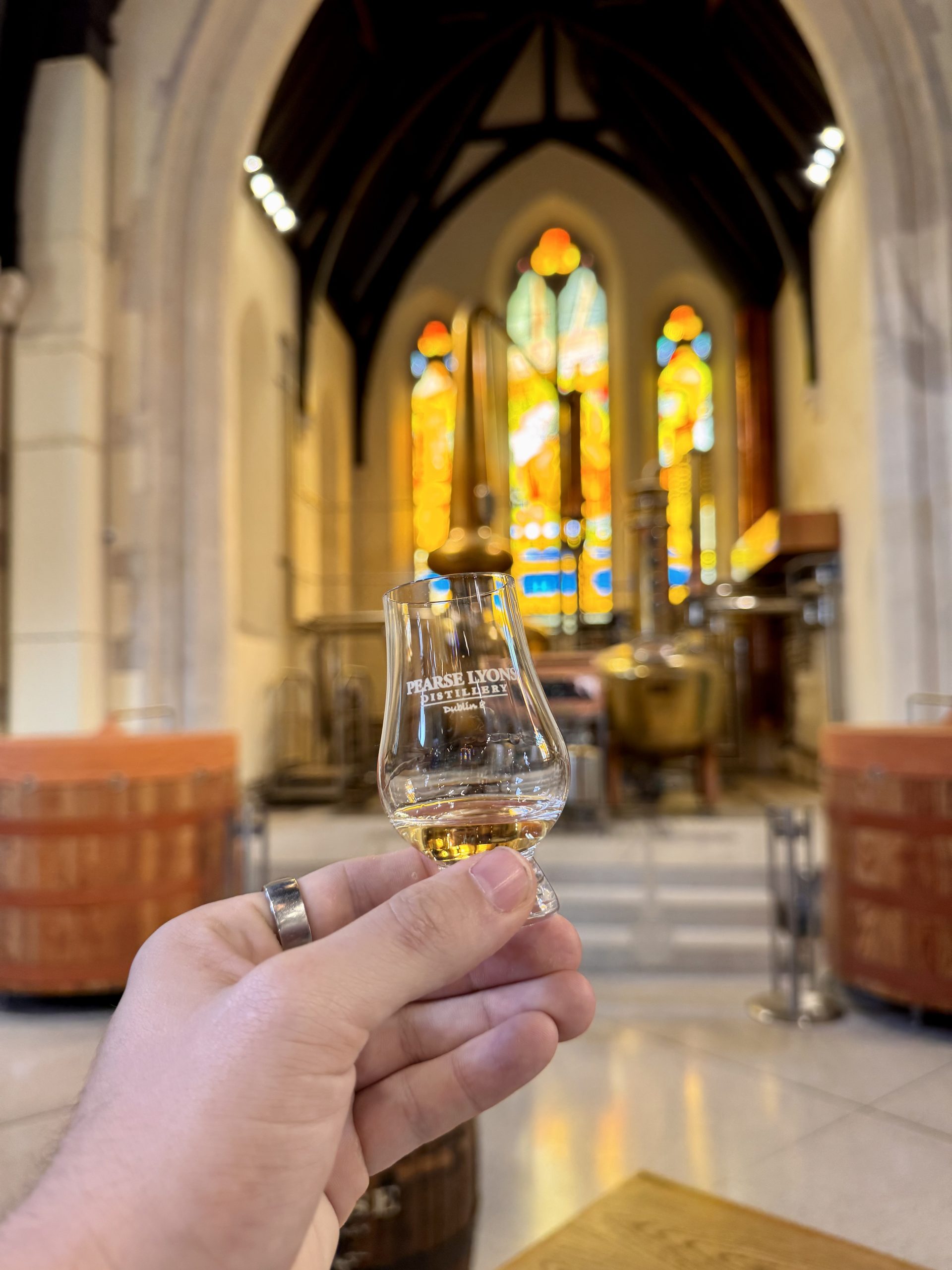A dram of Pearse Irish Whiskey held in front of the copper stills and stained glass, Pearse Lyons Distillery