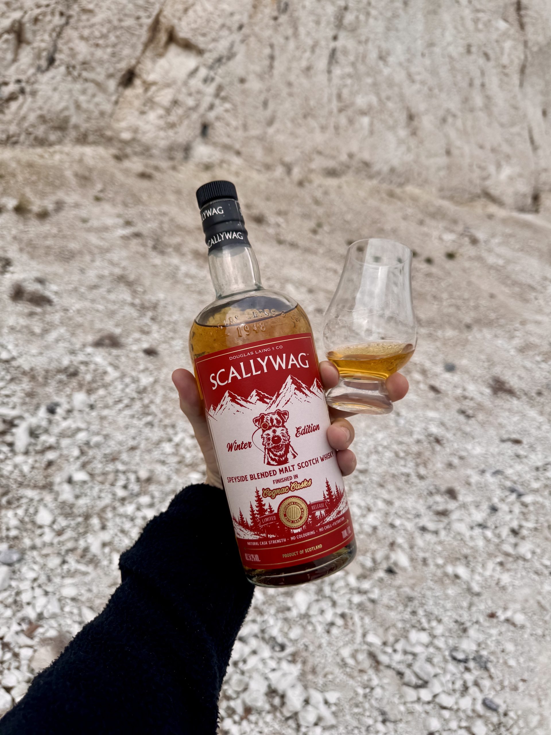 Hand holding a Scallywag Winter Edition 2026 bottle and a Glencairn glass of the Cognac cask Speyside malt in front of a white chalk cliff